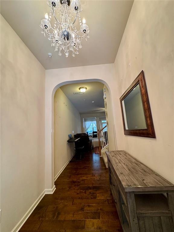 corridor featuring dark wood-style floors, arched walkways, a notable chandelier, and baseboards