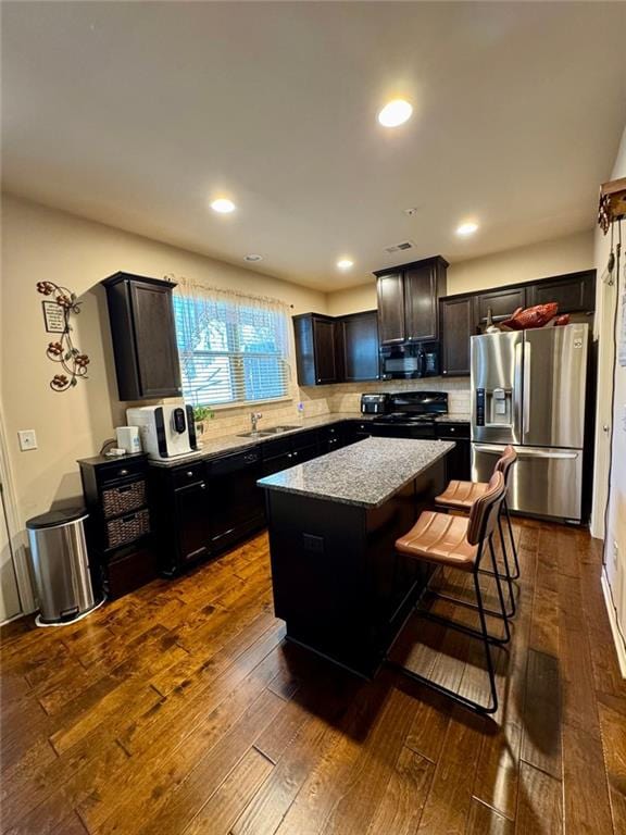 kitchen with a sink, black appliances, dark wood finished floors, and a center island