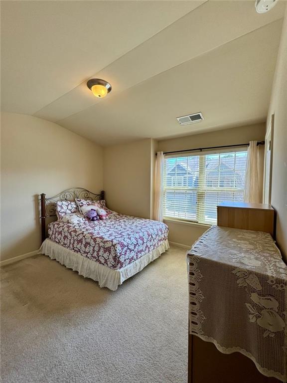 carpeted bedroom with visible vents, vaulted ceiling, and baseboards