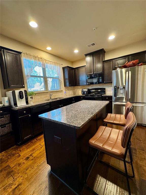 kitchen with dark wood-type flooring, a kitchen island, visible vents, dark stone counters, and black appliances