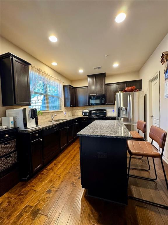 kitchen featuring tasteful backsplash, dark stone counters, dark wood-style floors, a kitchen island, and black appliances