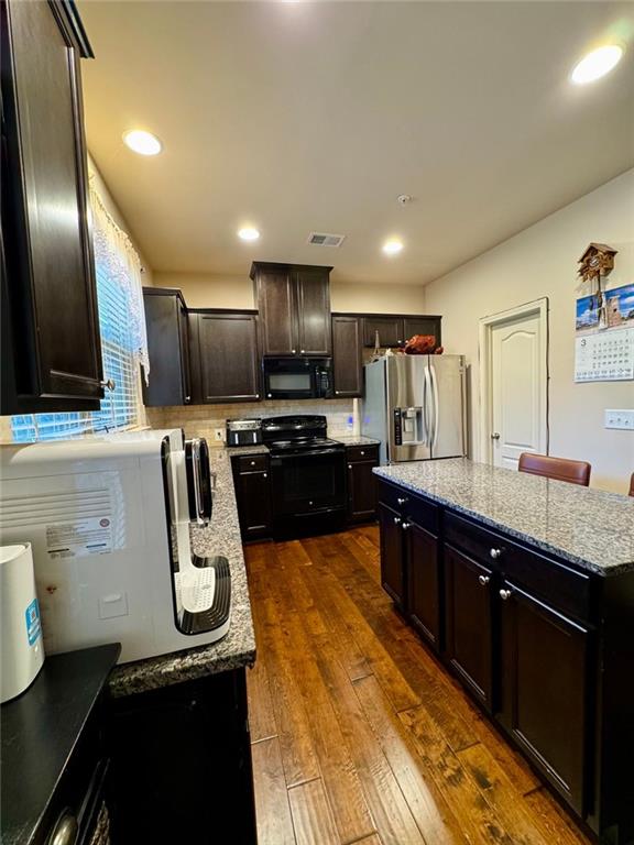 kitchen featuring light stone counters, dark wood-type flooring, a kitchen island, visible vents, and black appliances