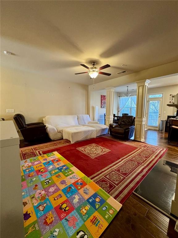 living area with decorative columns, visible vents, a ceiling fan, and wood finished floors