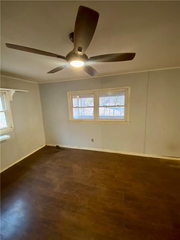 empty room featuring dark wood-style floors, crown molding, baseboards, and a ceiling fan