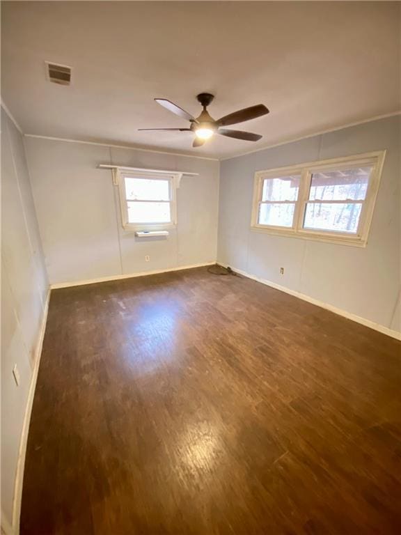 empty room with baseboards, visible vents, ceiling fan, dark wood-type flooring, and crown molding