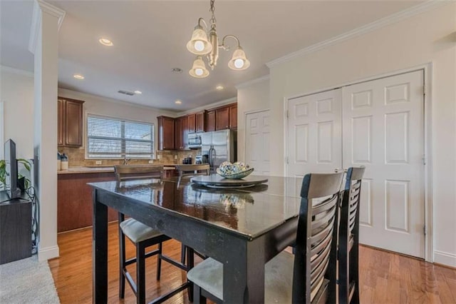 dining area with crown molding, a chandelier, and light hardwood / wood-style floors