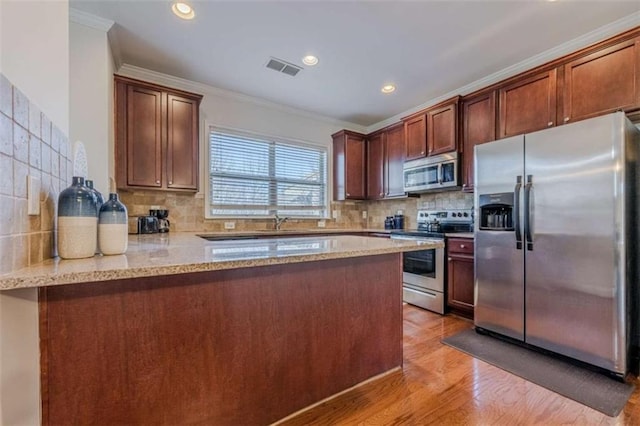 kitchen with stainless steel appliances, light stone countertops, ornamental molding, kitchen peninsula, and light wood-type flooring