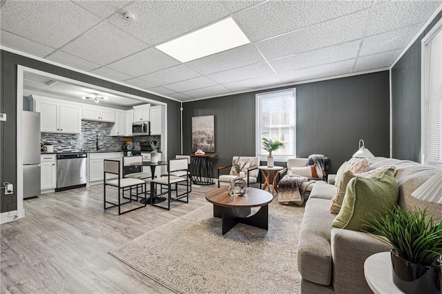 living room featuring sink, a drop ceiling, and light wood-type flooring