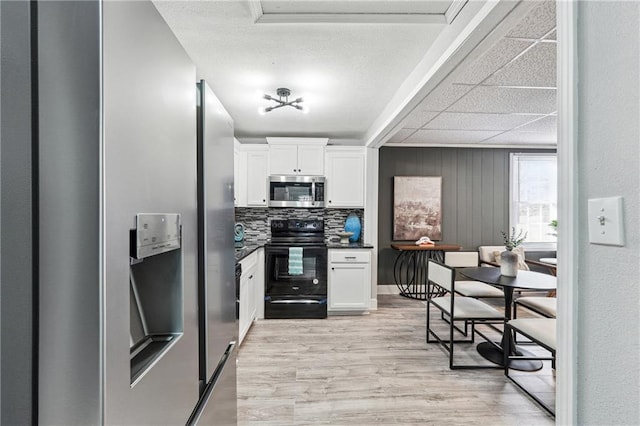 kitchen with stainless steel appliances, white cabinetry, backsplash, and light hardwood / wood-style flooring