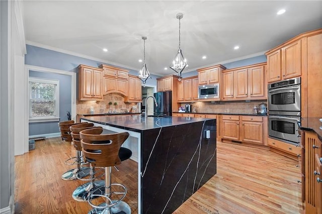 kitchen featuring sink, hanging light fixtures, appliances with stainless steel finishes, a kitchen breakfast bar, and a kitchen island with sink