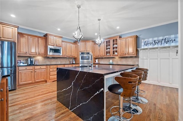 kitchen with crown molding, appliances with stainless steel finishes, a center island with sink, and a kitchen breakfast bar