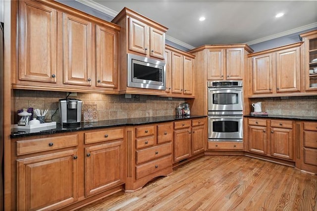 kitchen with ornamental molding, appliances with stainless steel finishes, dark stone countertops, and light hardwood / wood-style flooring