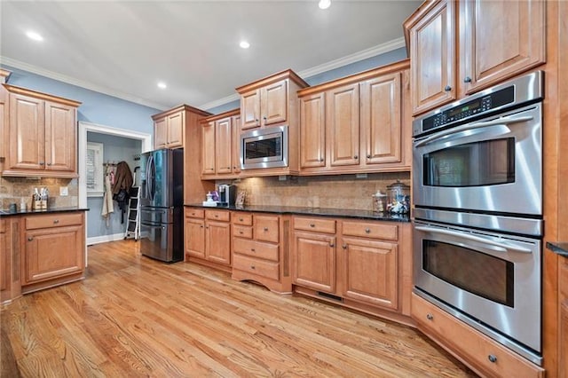 kitchen with appliances with stainless steel finishes, dark stone countertops, ornamental molding, light hardwood / wood-style floors, and decorative backsplash