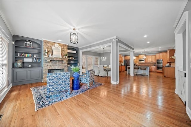 living room with crown molding, a notable chandelier, a fireplace, built in shelves, and light wood-type flooring