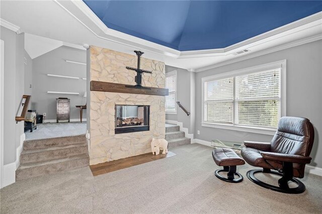 living area featuring vaulted ceiling, a stone fireplace, ornamental molding, a tray ceiling, and light carpet