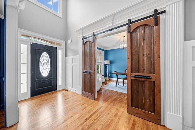 foyer featuring a towering ceiling, light hardwood / wood-style flooring, ornamental molding, and a barn door