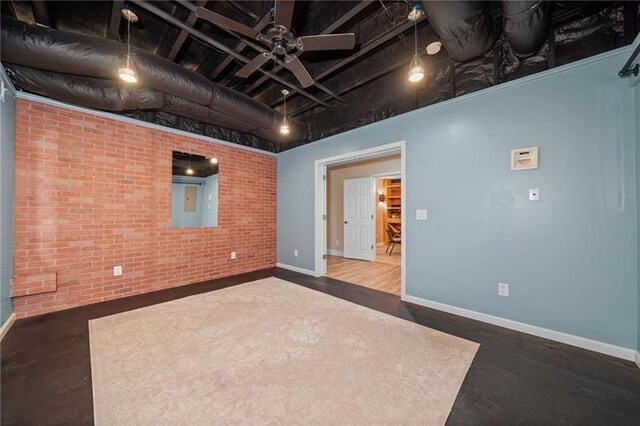 basement featuring dark wood-type flooring, ceiling fan, and brick wall