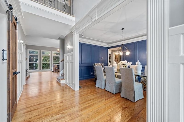 dining room with decorative columns, ornamental molding, a notable chandelier, light hardwood / wood-style floors, and a barn door