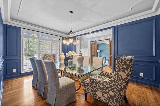 dining area featuring ornamental molding, a barn door, wood-type flooring, and a notable chandelier