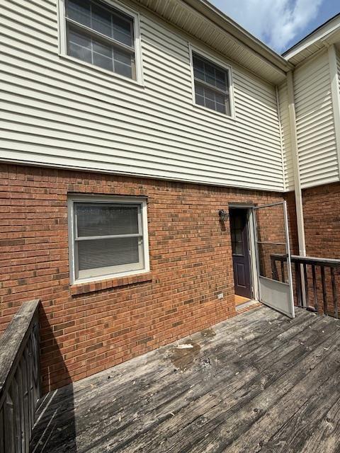 rear view of house featuring an attached garage, driveway, a deck, and brick siding