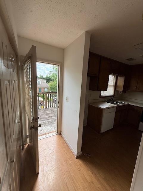 kitchen with white dishwasher, a sink, a textured ceiling, range with electric cooktop, and wood finished floors