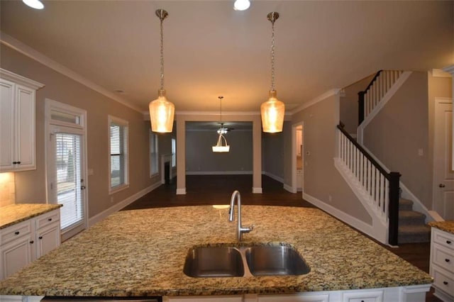 kitchen featuring light stone countertops, a kitchen island with sink, sink, and hanging light fixtures