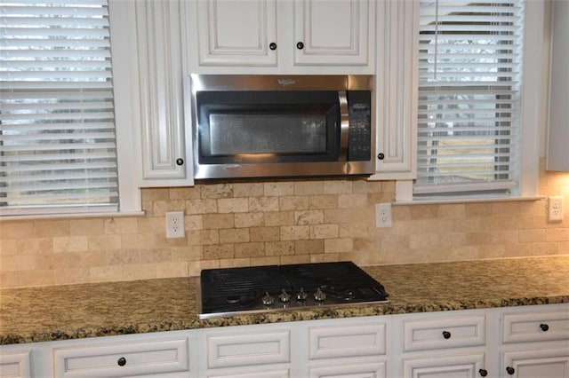 kitchen with backsplash, stainless steel appliances, white cabinetry, and dark stone counters