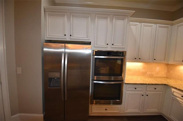 kitchen with light stone countertops, backsplash, stainless steel appliances, and white cabinetry