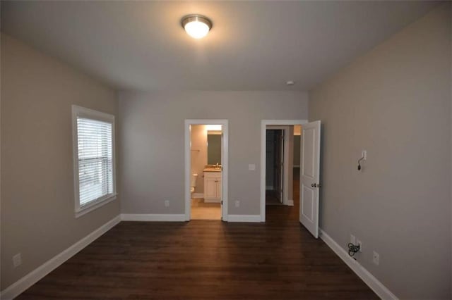 unfurnished bedroom featuring ensuite bathroom and dark hardwood / wood-style flooring