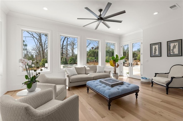 living room featuring crown molding, light wood-style flooring, plenty of natural light, and visible vents