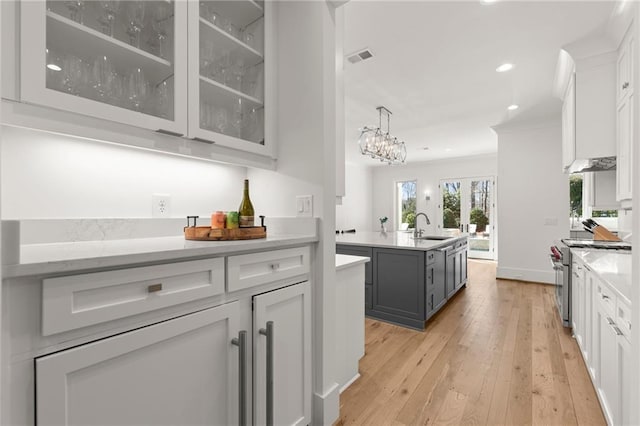 kitchen with a sink, stainless steel stove, light countertops, white cabinetry, and light wood-type flooring