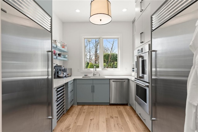 kitchen with light wood-style flooring, gray cabinets, a sink, stainless steel appliances, and light countertops