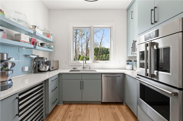 kitchen with gray cabinetry, light wood-style flooring, a sink, tasteful backsplash, and stainless steel appliances