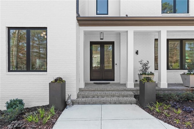 view of exterior entry featuring french doors, brick siding, and a porch