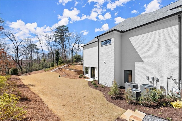 view of home's exterior with brick siding, central air condition unit, and driveway