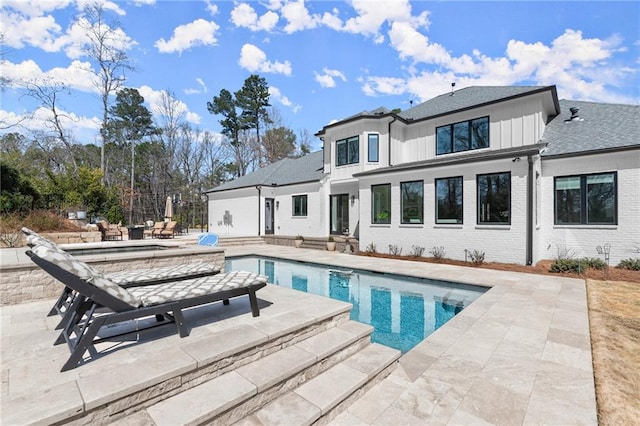 back of property with brick siding, board and batten siding, a shingled roof, an outdoor pool, and a patio