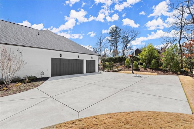 view of side of home with a garage, brick siding, driveway, and a shingled roof