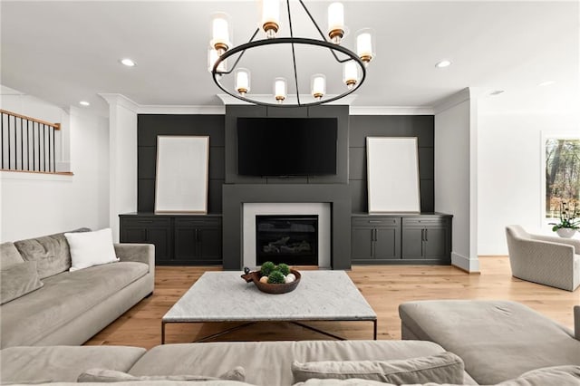 living area featuring light wood-style flooring, ornamental molding, a glass covered fireplace, recessed lighting, and a chandelier