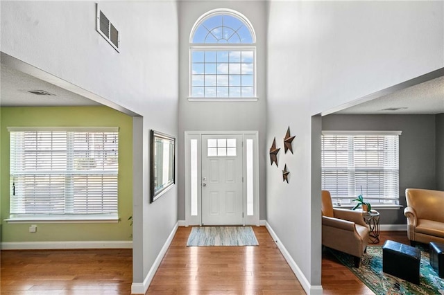 foyer with a high ceiling, wood finished floors, visible vents, and baseboards