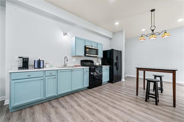 kitchen with black appliances, blue cabinets, light wood finished floors, and a sink