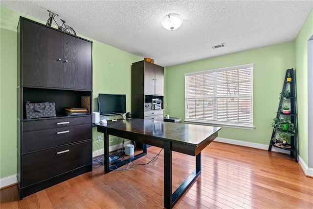 office space with visible vents, light wood-style flooring, a textured ceiling, and baseboards