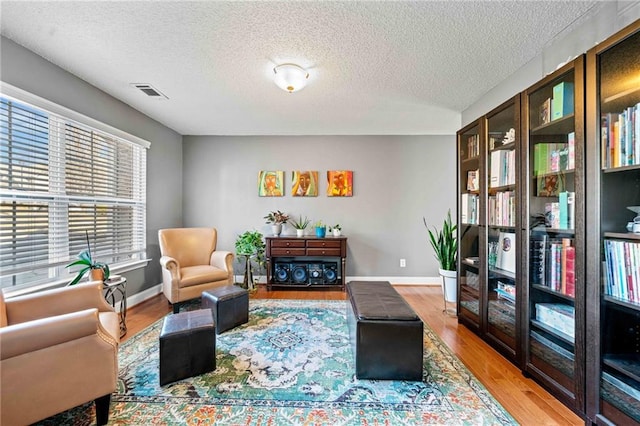 living room with visible vents, a textured ceiling, baseboards, and wood finished floors