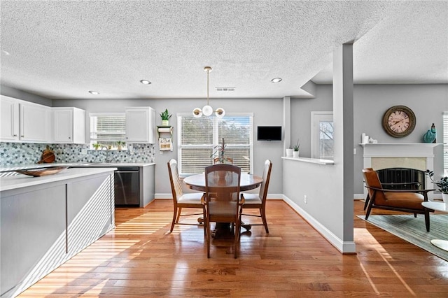 kitchen featuring light wood-style floors, tasteful backsplash, stainless steel dishwasher, and light countertops