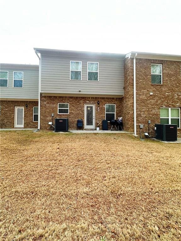 back of property with brick siding, central AC unit, and a lawn