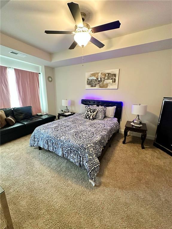 bedroom with visible vents, ceiling fan, baseboards, a tray ceiling, and carpet flooring