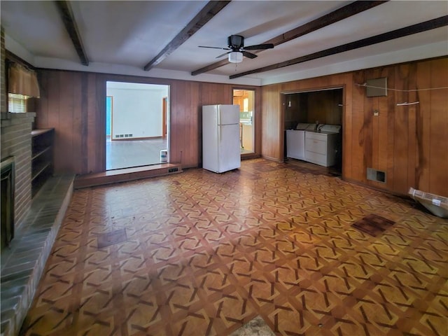 unfurnished living room with wooden walls, beamed ceiling, ceiling fan, a brick fireplace, and washer and clothes dryer