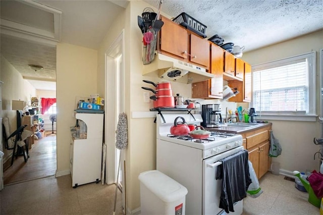 kitchen with brown cabinets, light floors, gas range gas stove, under cabinet range hood, and baseboards