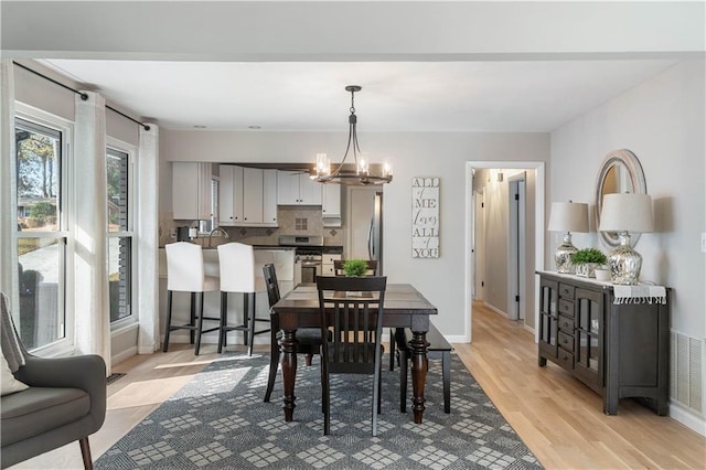 dining space with a notable chandelier, baseboards, visible vents, and light wood-type flooring