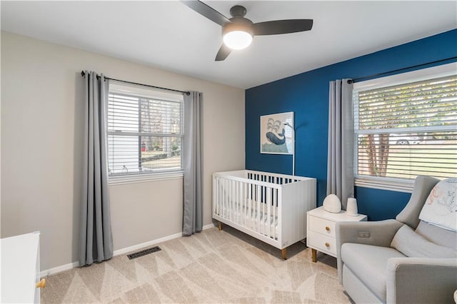 carpeted bedroom with visible vents, multiple windows, a crib, and baseboards