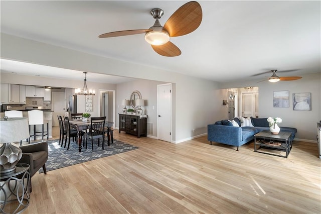 living room featuring baseboards, light wood-style flooring, and ceiling fan with notable chandelier